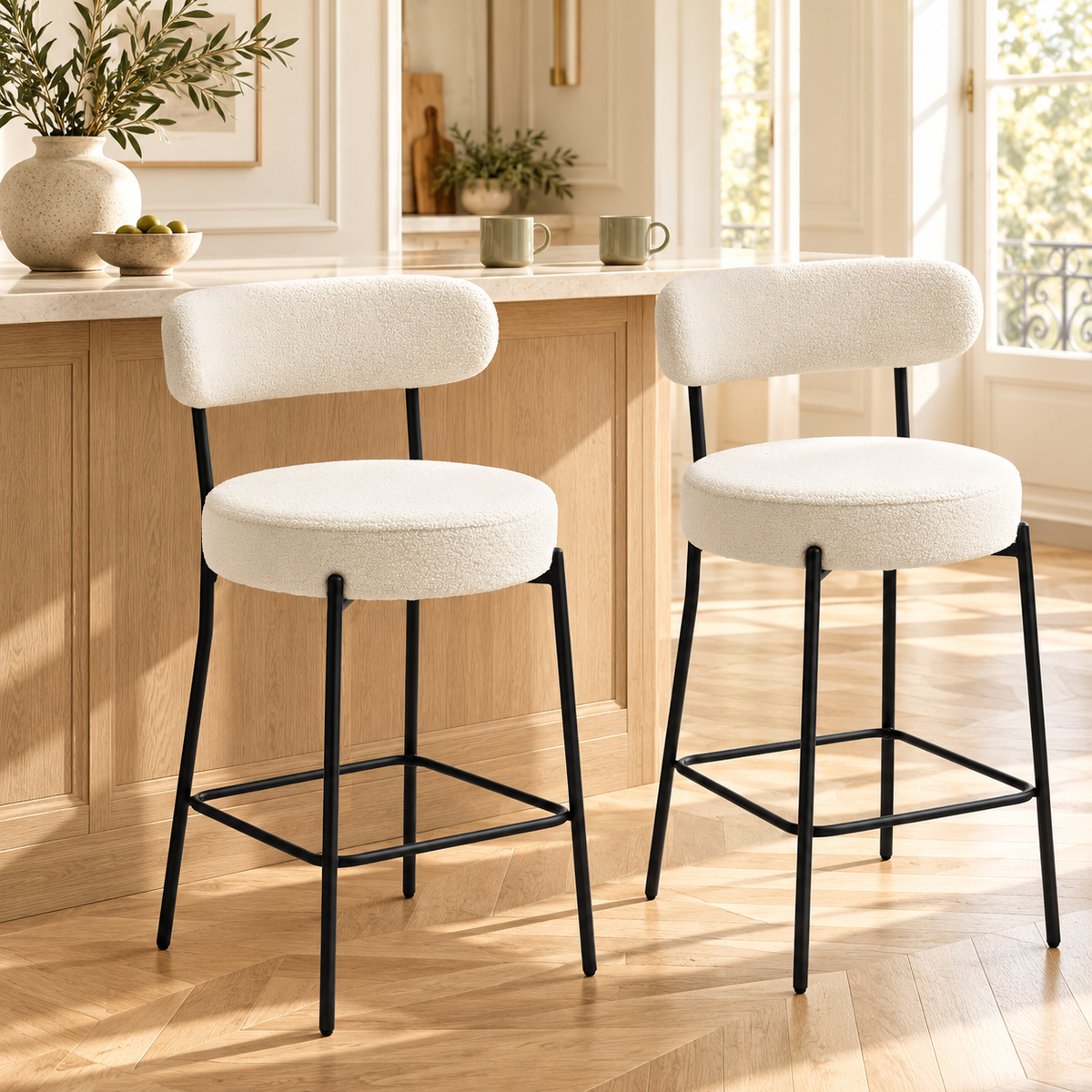 Deux tabourets bouclés crème devant un comptoir en bois clair et pierre dans une cuisine chaleureuse à moulures et parquet en chevrons.