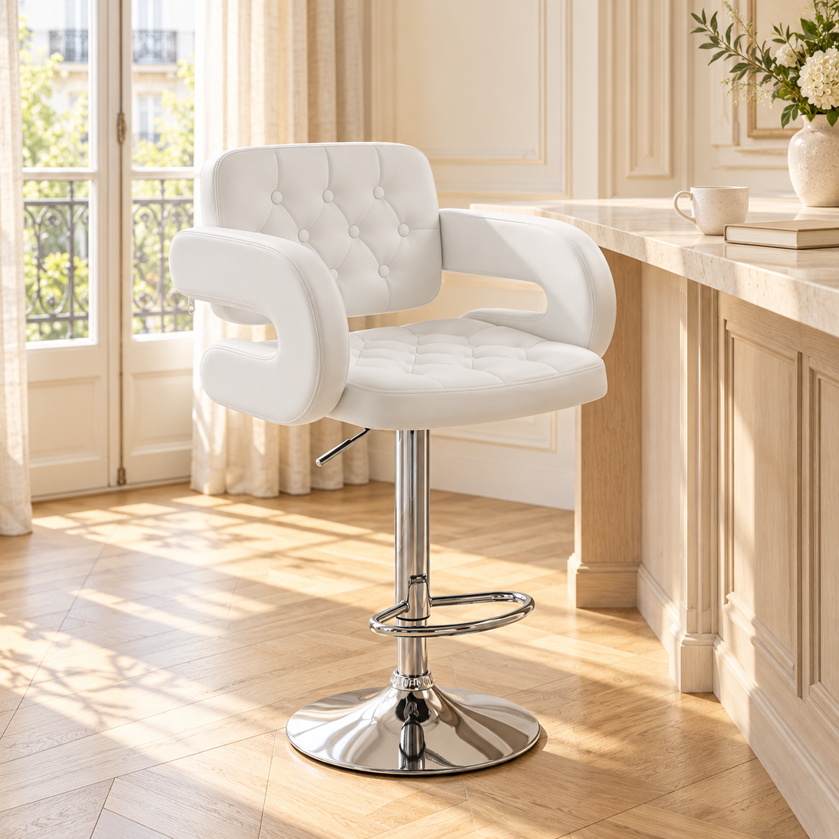 Fauteuil blanc capitonné à accoudoirs ouverts et pied chromé devant un comptoir en bois clair dans un intérieur lumineux à moulures.