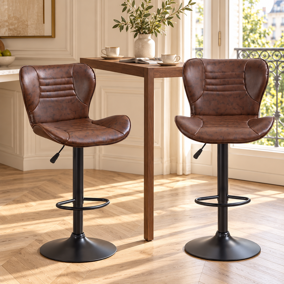 Deux fauteuils de bar marron à surpiqûres horizontales devant une table haute en bois dans un intérieur lumineux à moulures et parquet en chevrons.