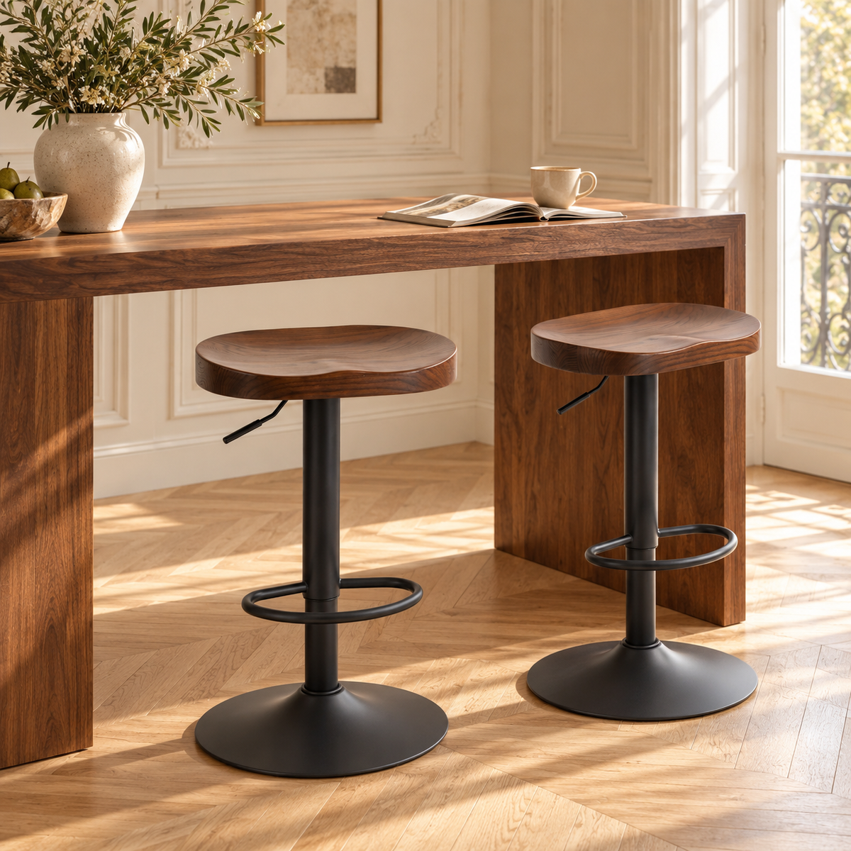 Deux tabourets de bar à assise incurvée en bois d’orme devant une console haute en bois, dans un intérieur lumineux à moulures et parquet clair.