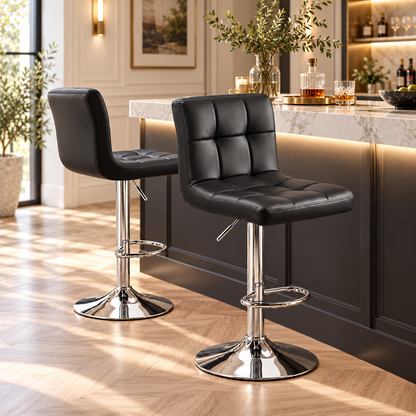 Deux tabourets de bar noirs réglables en similicuir installés devant un îlot de cuisine moderne et lumineux.
