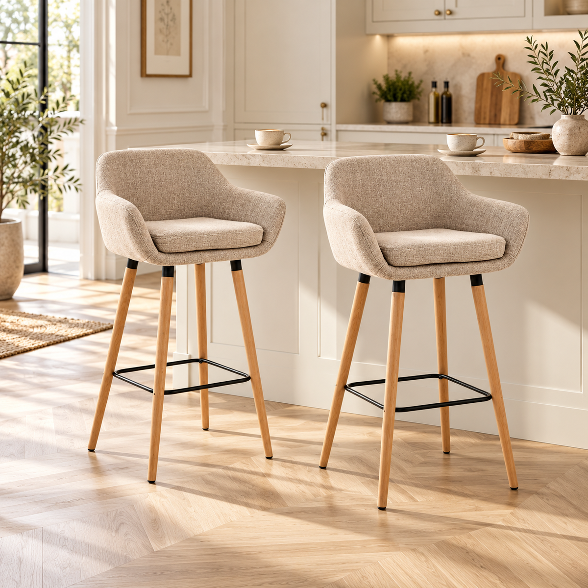 Lot de deux tabourets de bar scandinaves beiges avec accoudoirs et pieds en bois devant un comptoir de cuisine crème, dans un intérieur chaleureux et lumineux.
