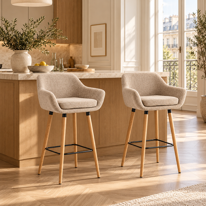 Deux tabourets de bar scandinaves beiges à accoudoirs devant un îlot en bois et pierre dans une cuisine lumineuse avec parquet en chevrons.